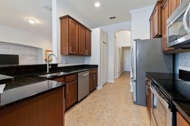 kitchen with sink, dark stone countertops, ornamental molding, appliances with stainless steel finishes, and backsplash