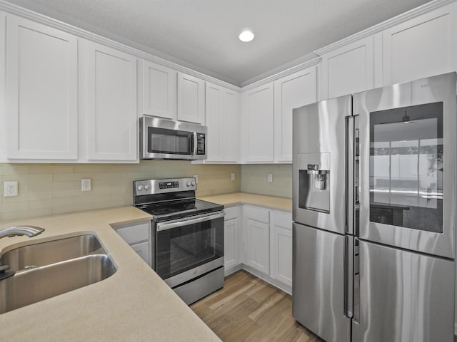 kitchen with backsplash, light wood-type flooring, stainless steel appliances, sink, and white cabinetry