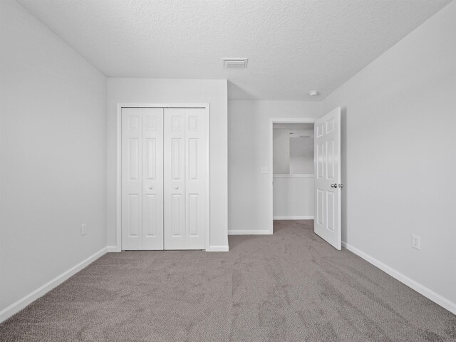 unfurnished bedroom with light colored carpet, a textured ceiling, and a closet