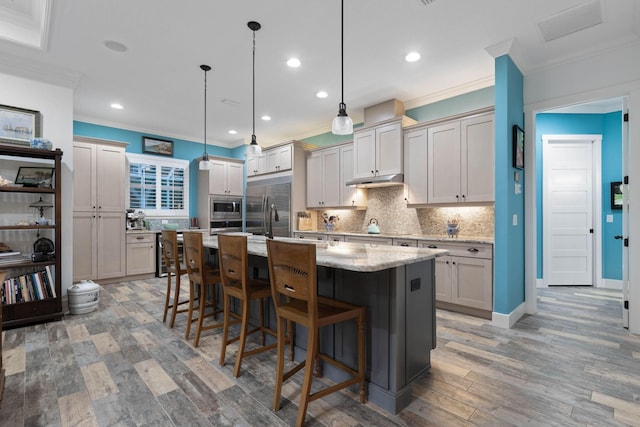 kitchen with built in appliances, an island with sink, decorative light fixtures, a kitchen bar, and hardwood / wood-style flooring