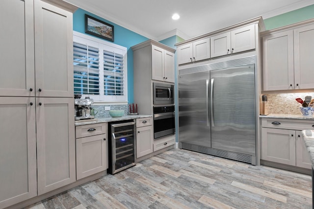 kitchen with built in appliances, decorative backsplash, ornamental molding, light stone counters, and beverage cooler