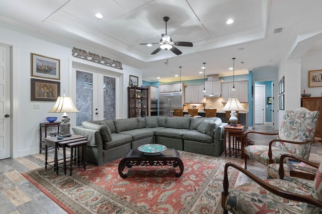 living room featuring french doors, light wood-type flooring, a raised ceiling, and crown molding