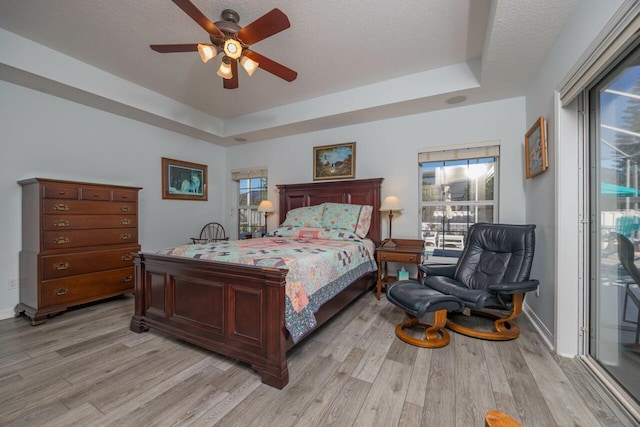 bedroom featuring ceiling fan, a raised ceiling, light hardwood / wood-style floors, a textured ceiling, and access to outside