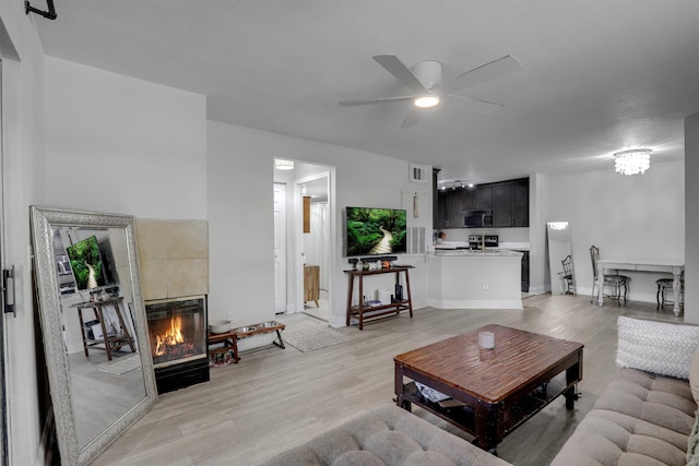 living room featuring hardwood / wood-style floors, ceiling fan with notable chandelier, and a tiled fireplace