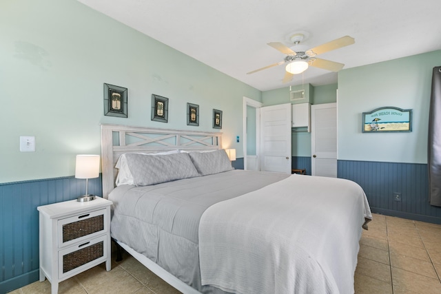 bedroom with tile patterned floors, wainscoting, visible vents, a ceiling fan, and wooden walls