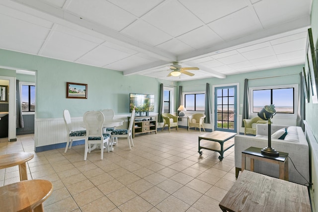 living room with light tile patterned floors, beamed ceiling, wainscoting, and ceiling fan