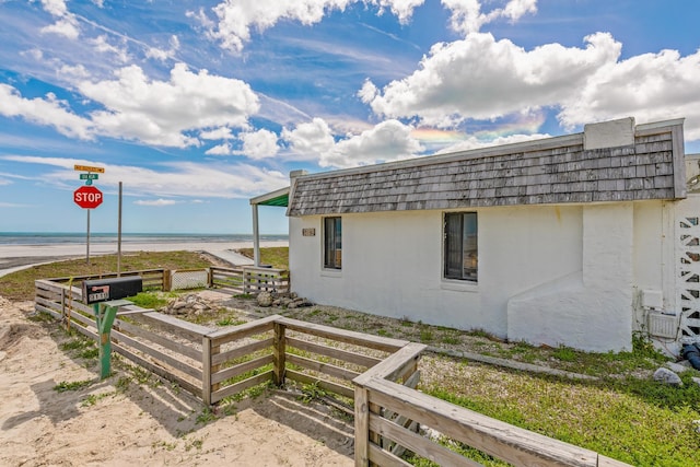 view of property exterior featuring a view of the beach, a water view, stucco siding, and fence
