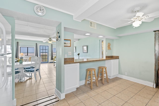 kitchen featuring dark countertops, light tile patterned flooring, ceiling fan, beam ceiling, and visible vents