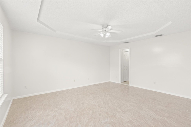 empty room featuring a raised ceiling, ceiling fan, and a textured ceiling