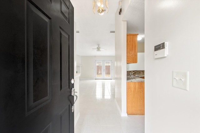 hall featuring light tile patterned flooring, sink, a notable chandelier, a textured ceiling, and french doors