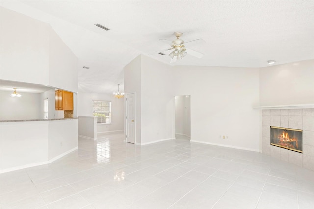 unfurnished living room with light tile patterned flooring, lofted ceiling, a textured ceiling, a tiled fireplace, and ceiling fan with notable chandelier