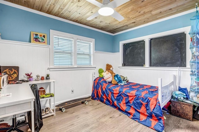 bedroom with wood finished floors, a wainscoted wall, ceiling fan, crown molding, and wooden ceiling