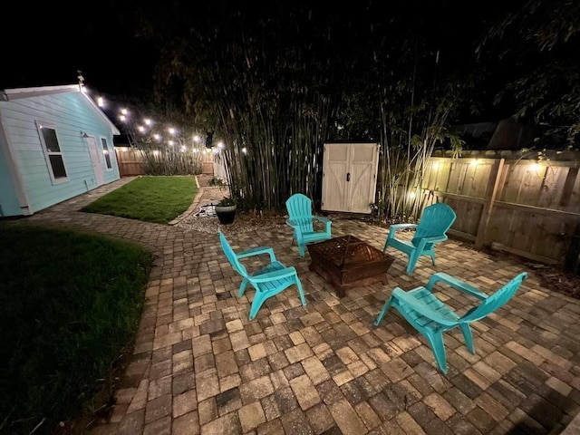 patio at night featuring an outdoor fire pit, a lawn, a fenced backyard, an outbuilding, and a storage unit