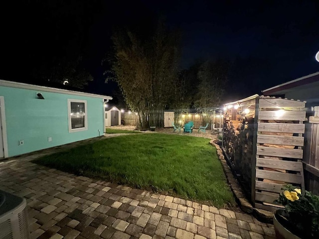 yard at night featuring an outdoor structure, a storage unit, a fenced backyard, and central AC