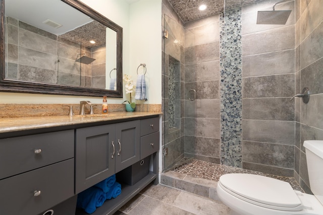 bathroom with toilet, visible vents, tiled shower, and vanity