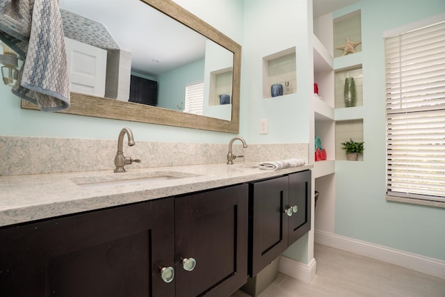 bathroom with a sink, baseboards, and double vanity