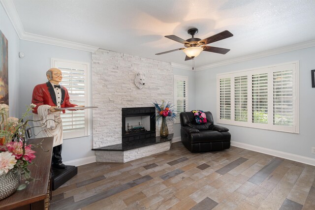 living area featuring crown molding, a fireplace, a ceiling fan, wood finished floors, and baseboards