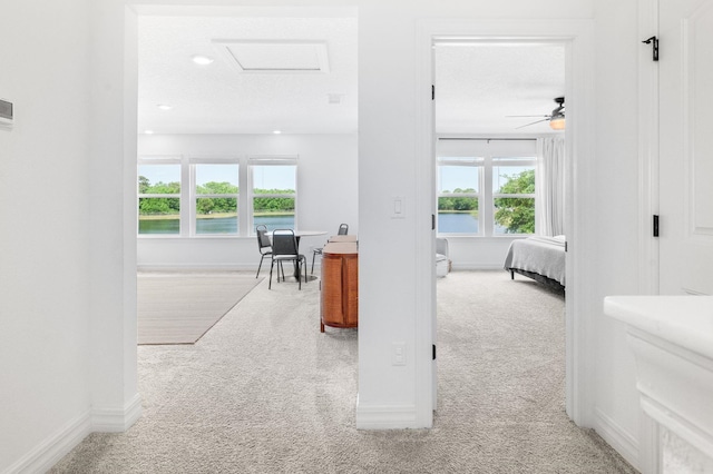 hallway with carpet floors, baseboards, recessed lighting, attic access, and a water view