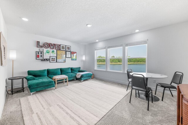living area with carpet flooring, a water view, a textured ceiling, recessed lighting, and baseboards