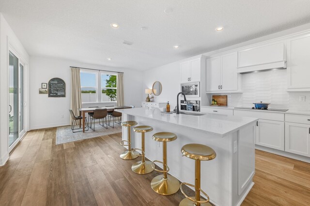 kitchen with a sink, light countertops, an island with sink, tasteful backsplash, and a breakfast bar