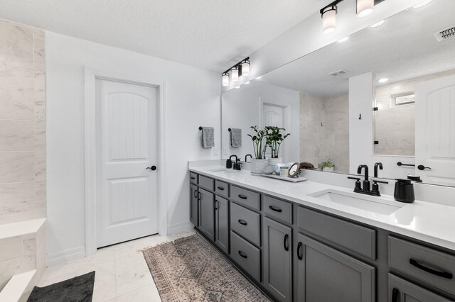 bathroom featuring tiled shower, double vanity, baseboards, a textured ceiling, and marble finish flooring