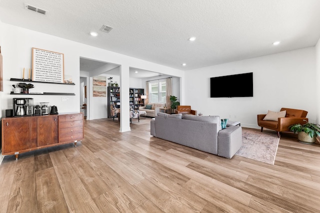 living room with light wood-style floors, recessed lighting, a textured ceiling, and a bar