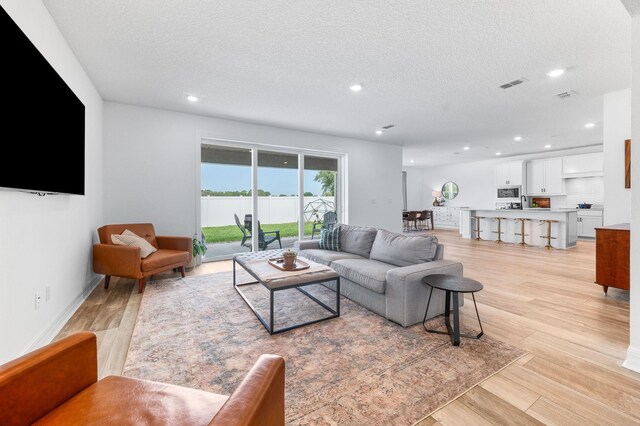 living area featuring light wood finished floors, a textured ceiling, recessed lighting, and baseboards
