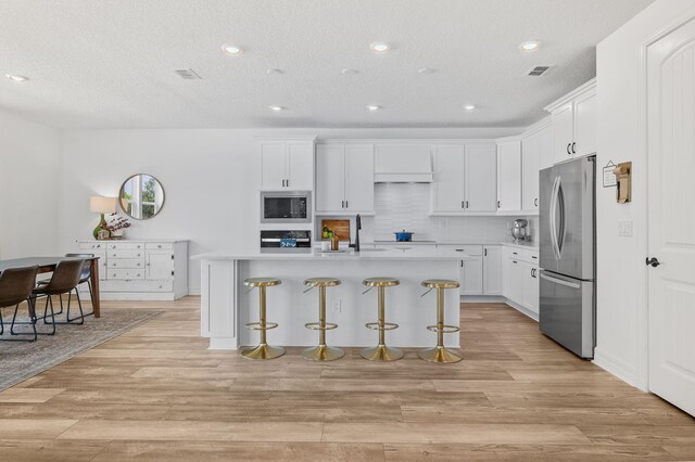 kitchen featuring stainless steel appliances, a sink, a kitchen breakfast bar, light countertops, and recessed lighting