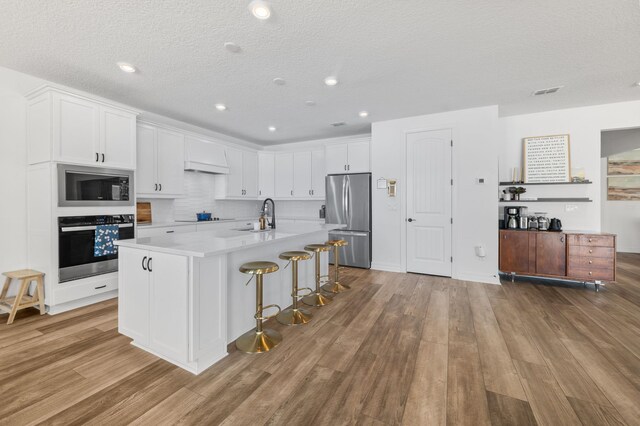 kitchen featuring black appliances, a sink, white cabinets, light countertops, and wood finished floors