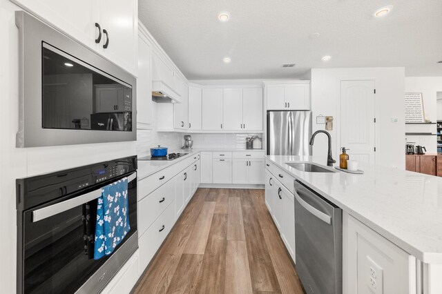 kitchen with stainless steel appliances, a sink, light wood finished floors, white cabinetry, and recessed lighting