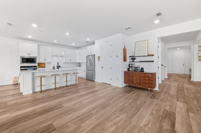 kitchen featuring appliances with stainless steel finishes, a kitchen breakfast bar, light wood-style flooring, light countertops, and recessed lighting