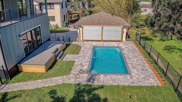 view of swimming pool featuring a lawn, a wooden deck, an outbuilding, and a patio