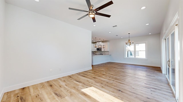 unfurnished living room featuring ceiling fan with notable chandelier and light wood-type flooring