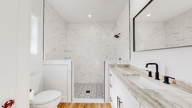 bathroom with hardwood / wood-style floors, toilet, a tile shower, and vanity