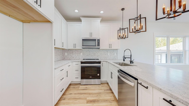 kitchen featuring sink, light stone counters, decorative light fixtures, appliances with stainless steel finishes, and light wood-type flooring