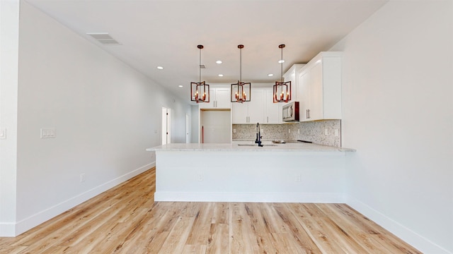 kitchen with white cabinets, decorative light fixtures, light hardwood / wood-style floors, and backsplash