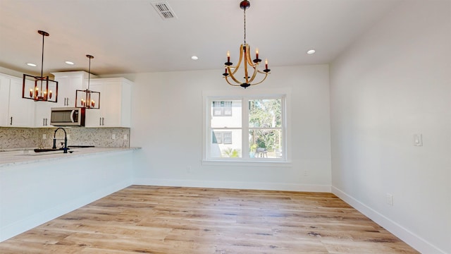 unfurnished dining area featuring a chandelier, sink, and light hardwood / wood-style floors