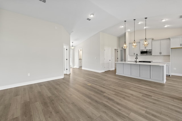 kitchen with decorative light fixtures, backsplash, sink, light hardwood / wood-style flooring, and a kitchen island with sink