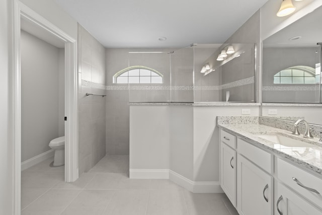 bathroom featuring tile patterned floors, vanity, a tile shower, and toilet