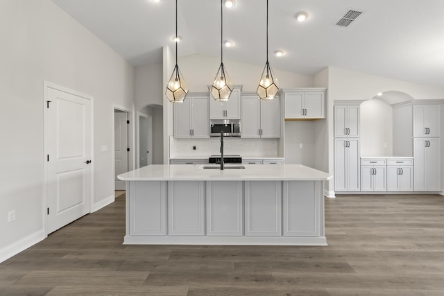 kitchen with lofted ceiling, a center island with sink, decorative backsplash, white cabinetry, and hanging light fixtures