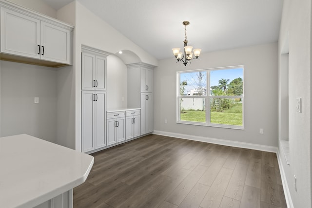 unfurnished dining area with vaulted ceiling, a chandelier, and dark hardwood / wood-style floors