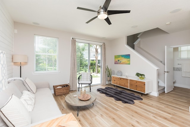 living room featuring ceiling fan, stairway, light wood-type flooring, and baseboards