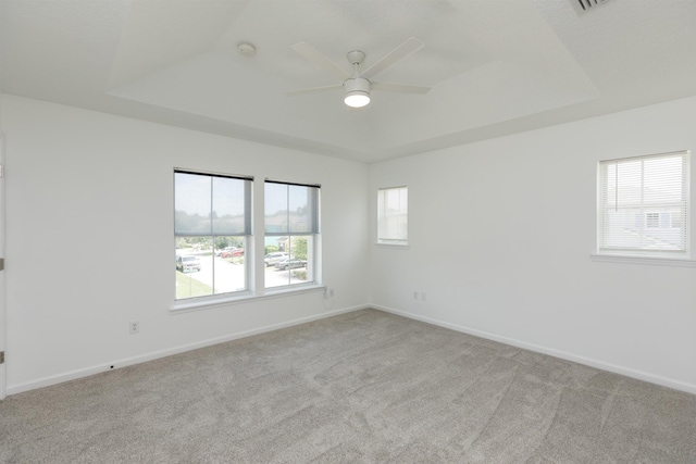 carpeted spare room with a tray ceiling, ceiling fan, and baseboards