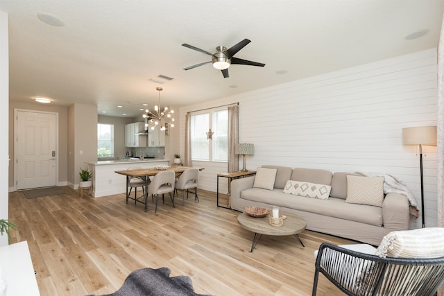 living room with light wood-type flooring, visible vents, baseboards, and ceiling fan with notable chandelier