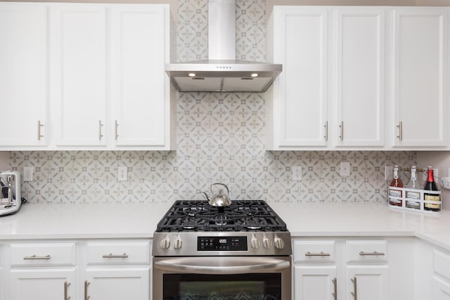 kitchen with wall chimney exhaust hood, stainless steel range with gas cooktop, light countertops, and white cabinetry