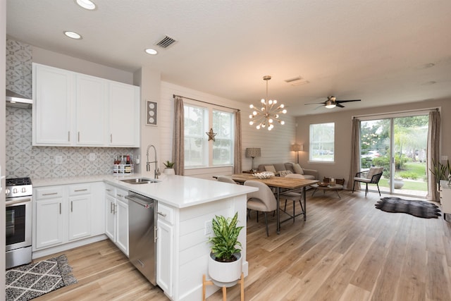 kitchen featuring stainless steel appliances, light wood-style flooring, open floor plan, a sink, and a peninsula