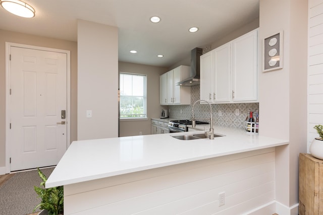 kitchen featuring light countertops, backsplash, a sink, wall chimney range hood, and a peninsula