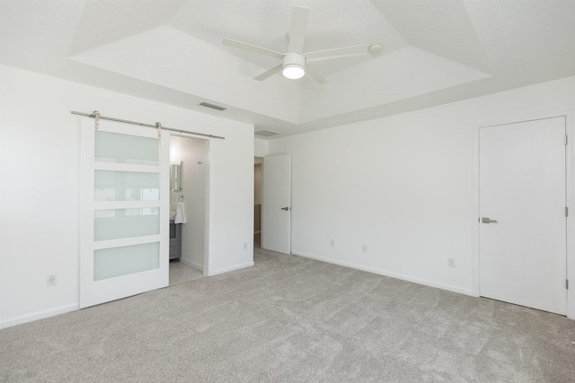 unfurnished bedroom featuring a barn door, carpet flooring, visible vents, a raised ceiling, and ensuite bath