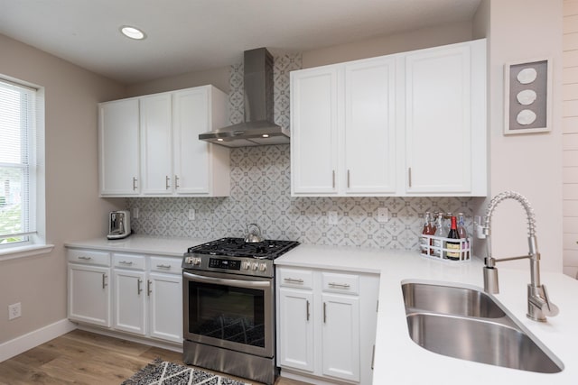 kitchen featuring a sink, wall chimney range hood, stainless steel range with gas cooktop, and decorative backsplash