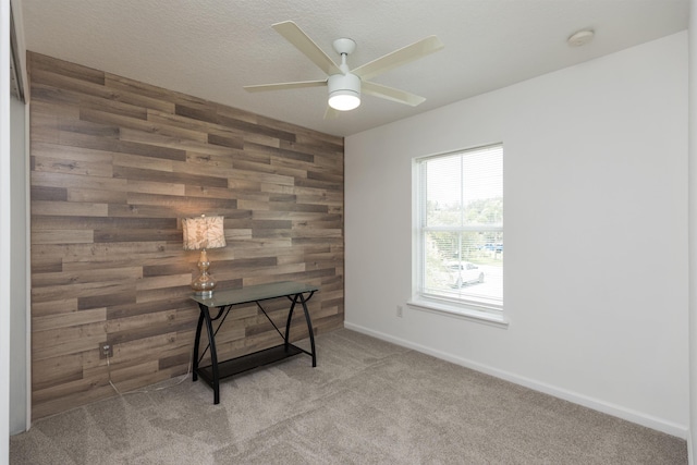 carpeted office with an accent wall, a ceiling fan, wood walls, a textured ceiling, and baseboards